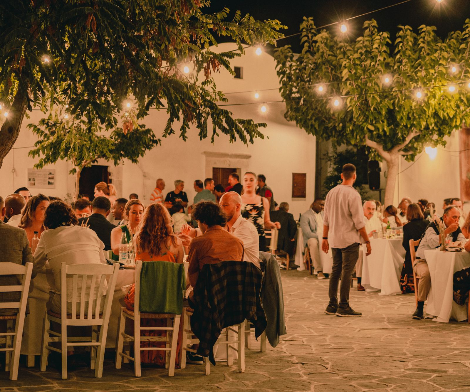 Des convives partagent un repas en plein air sous des guirlandes lumineuses